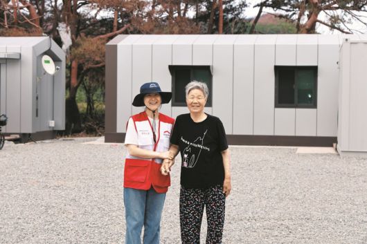 희망브리지 - 경상북도 청송군 희망하우스 앞에서 김분순 어르신(오른쪽)이 희망브리지 직원과 함께 환하게 웃고 있다. /희망브리지 제공