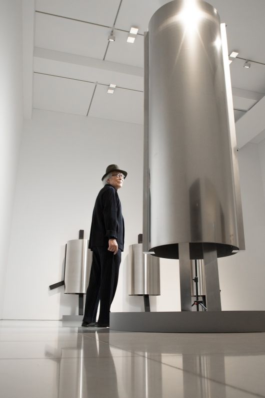 엄태정 조각가가 은빛 원통형 조각 ‘낯선 자의 은신처’ 사이에 서 있다. 알루미늄으로 만든 신작 연작이다. /고운호 기자