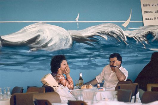 볼로냐의 한 식당 벽에 그려진 파도 그림. 아래 테이블에 무료한 표정의 손님들과 묘한 대조를 이룬다. Bologna, f11, 1125, Natural Light series, 1973, C-print, 23.8×34.8cm, © Heirs of Luigi Ghirri