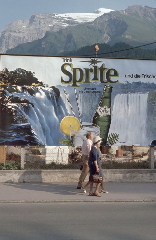 스위스 휴양지 엥겔베르크에서 촬영한 사진으로 담 너머 알프스 산들이 보이고 스프라이트 광고 사진은 마치 빙하에서 녹은 폭포처럼 보인다. Engelberg, Kodachrome series, 1972, C-print, 21.8×14cm, © Heirs of Luigi Ghirri