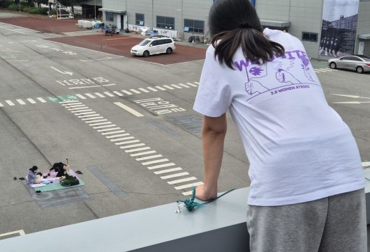 고공농성 500일을 열흘 앞둔 2025년 5월11일, 박정혜씨와 연대하러 온 시민들이 돗자리를 펴고 앉아 손을 흔들자 박정혜씨가 이들을 바라보고 있다. 신다은 기자