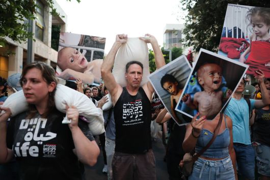 이스라엘과 아랍 활동가들이 밀가루 포대를 지고 굶주린 가자 어린이들의 사진을 들고 가자 전쟁과 그로 인한 기아를 모두 끝내자고 요구하며 22일 이스라엘 텔아비브 시내를 행진하고 있다. EPA 연합뉴스