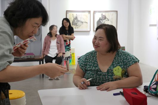 정은혜 작가(오른쪽)가 8월22일 오후 경기 양평군 강상면 어메이징 아웃사이더 아트센터 전시장에서 관람객들에게 사인을 해주자 관람객이 “너무 작품 같은 사인”이라며 감탄하고 있다. 정용일 선임기자 yongil@hani.co.kr