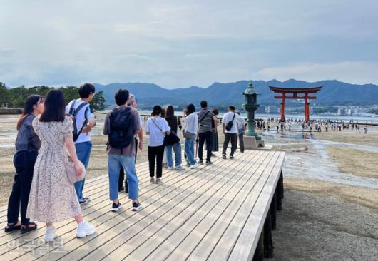 관광객이 이쓰쿠시마 신사에서 도리이를 배경으로 기념사진을 찍기 위해 길게 줄을 서 있다.