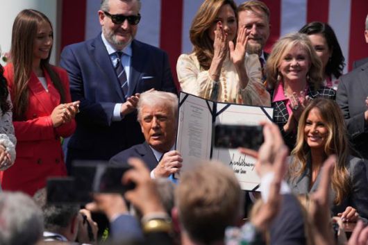 도널드 트럼프(가운데) 미국 대통령이 19일 워싱턴 백악관 로즈가든에서 영부인 멜라니아 여사와 자신이 서명을 마친 테이크 잇 다운 법을 들어 보이고 있다. 워싱턴=AP 연합뉴스