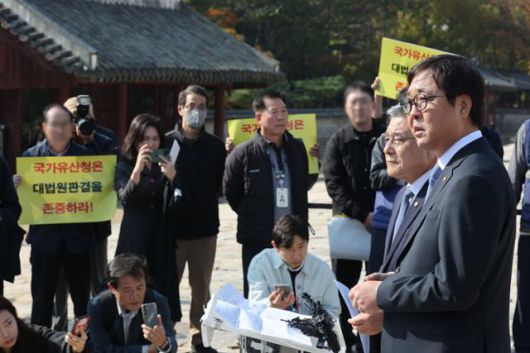 최휘영(오른쪽) 문화체육관광부 장관과 허민 국가유산청장이 7일 서울 종묘에서 종묘 앞 개발 규제 완화 관련 대법원 판결에 대한 입장 발표 기자회견을 진행하는 가운데 세운4구역 주민 대표들이 개발 지연에 항의하는 피켓을 들고 있다. 연합뉴스