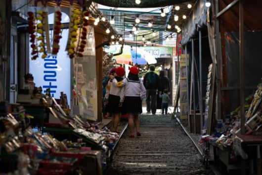 철길 양옆으로 상인들의 물건이 잔뜩 쌓여 있는 가운데 관광객이 교복을 입고 기념촬영을 하고 있다.
