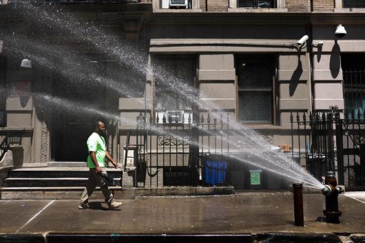 25일(현지시간) 뉴욕시 맨해튼 자치구에서 한 남성이 물을 뿌리는 소화전을 지나고 있다. [AFP]