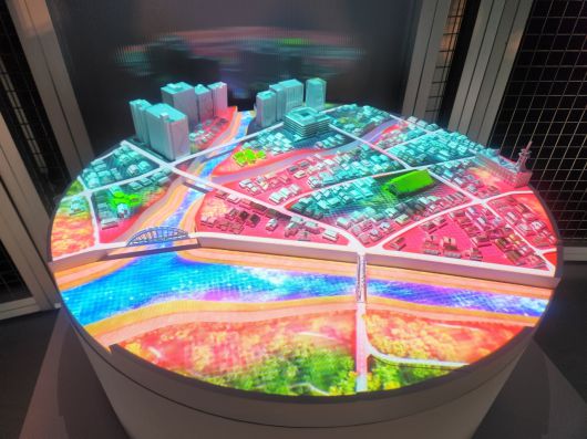 오사카 엑스포 내 네이버클라우드 부스에 설치 된 디지털트윈을 활용한 홍수 조감도(왼쪽 사진). 빨간 부분이 홍수로 피해를 볼 것으로 예상되는 지역이다. 고재우 기자