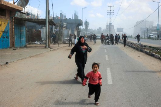 가자지구에서 한 여성이 지난 19일(현지시간) 이스라엘군의 공습에서 벗어나고자 한 소녀와 함께 거리로 달려나오고 있다. [AFP]