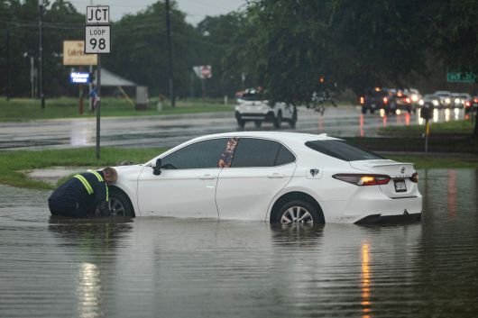 13일 텍사스 잉그램에서 대형 견인차 기사가 도로에 물에 잠긴 자동차에 케이블을 연결하려 하고 있다.[AFP]