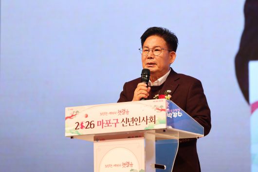 박강수 마포구청장이 마포구 신년인사회에서 마이크를 잡고 연설하고 있는 모습이다. 연설대에는 ‘함께 만드는 변화, 눈부신 마포’라는 문구와 함께 ‘2026 마포구 신년인사회’라는 텍스트가 적혀 있다.