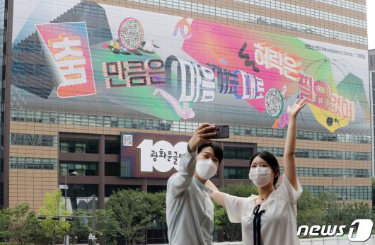 30일 오전 서울 종로구 교보빌딩에 100번째 광화문글판 '춤 만큼은 마음 가는 대로, 허락은 필요 없어'을 배경으로 시민들이 사진을 찍고 있다. 글로벌 아티스트 방탄소년단(BTS)가 100번째 광화문글판을 위해 문안 제작에 참여한 이번 글판은 코로나 펜데믹으로 제약이 늘고 고단한 하루 속에서도 허락받지 않고 자유로움을 느낄 수 있는 것을 찾자는 메시지를 담았다. 2021.8.30/뉴스1 © News1 박세연 기자