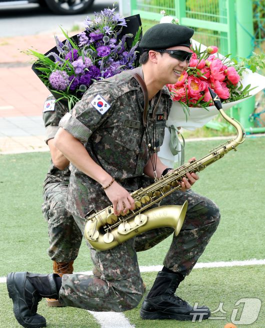 방탄소년단(BTS)의 뷔(김태형, 29)가 10일 오전 강원도 춘천시 신북읍 체육공원 축구장에서 섹소폰 연주를 하는 RM 뒤에서 꽃다발을 들고 그의 제대를 축하하고 있다. 2025.6.10/뉴스1 ⓒ News1 권현진 기자