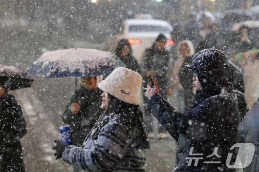 첫눈이 내린 4일 오후 서울 중구 명동을 찾은 관광객들이 내리는 눈을 맞으며 즐거워하고 있다. 기상청은 "퇴근 시간대 강한 눈이 내릴 가능성이 크다＂며 동네 예보와 실시간 날씨를 확인할 것을 당부했다. 2025.12.4/뉴스1 ⓒ News1 박정호 기자">