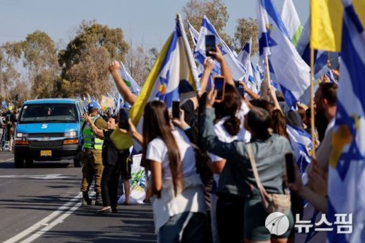 이스라엘 생존 인질을 실은 차량이 13일(현지 시간) 이스라엘 남부에 있는 군기지를 향해 달려가자 시민들이 국기를 흔들며 환영하고 있다. [사진=로이터 뉴스핌]