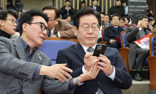 더불어민주당 이재명 대표가 지난 24일 국회에서 열린 의원총회에서 김민석 최고위원이 건넨 휴대폰을 보고 있다. 연합뉴스