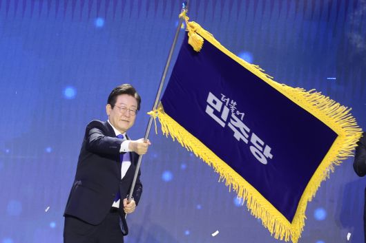 지난해 8월 열린 더불어민주당 전당대회에서 당대표 재선에 성공한 뒤 당 깃발을 흔드는 모습.   연합뉴스