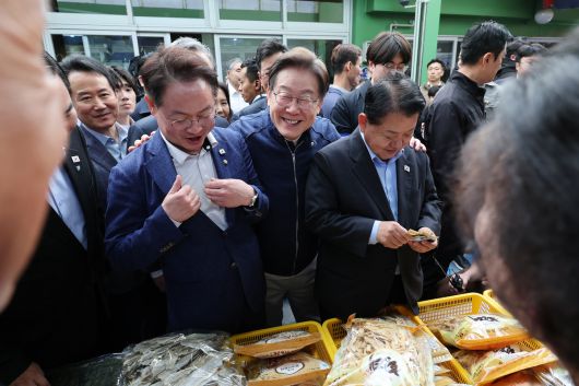 민심을 청취하는 '경청 투어'에 나선 이재명 더불어민주당 대선후보가 2일 오후 강원도 인제군 원통전통시장에서 건어물 가게를 방문해 황태채를 맛본 뒤 허영(왼쪽), 김병주 의원에게 구입을 권하고 있다.   뉴시스