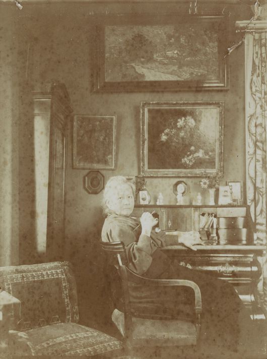 거실 책상 앞의 요 반 고흐 봉어르. 1909년 혹은 그 이후 암스테르담 집에서 찍은 사진으로 책상 뒤편 벽에 판탱라투르의 ‘꽃’과 빈센트 반 고흐의 ‘은선초 꽃병’, ‘황혼풍경(위)’이 보인다. 아트북스 제공