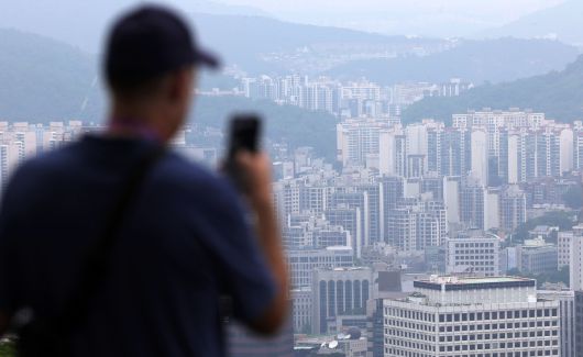 서울 도심의 아파트 단지를 배경으로 한 시민이 스마트폰으로 풍경을 촬영하고 있다. 정부가 6월 27일 발표한 ‘가계부채 관리 강화 방안’에 따라 수도권 주택담보대출이 대폭 제한되면서, 주택 매매시장에 다시 긴장감이 감돌고 있다. 뉴시스