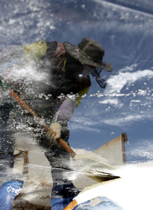 염부 전동길 씨가 결정지에서 소금삽을 들고 소금을 긁어모으고 있다. 사진은 결정지에 반영된 전동길씨 모습이다.