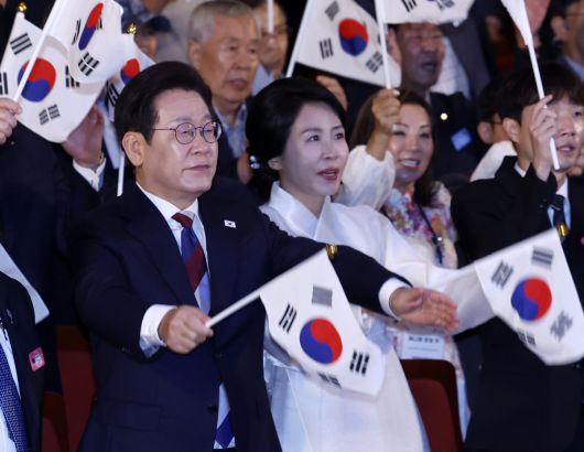 이재명 대통령과 김혜경 여사가 15일 서울 종로구 세종문화회관에서 열린 제80주년 광복절 경축식에서 참석자들과 태극기를 흔들고 있다. 뉴시스