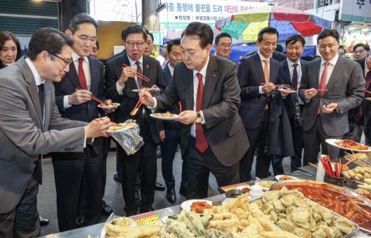 윤석열 대통령이 6일 부산 중구 깡통시장을 방문해 박형준 부산시장과 이재용 삼성전자 회장, 구광모 LG그룹 회장, 조현준 효성그룹 회장, 김동관 한화그룹 부회장, 최재원 SK수석부회장 등 기업총수들과 함께 떡볶이, 튀김, 빈대떡을 맛보고 있다. 2023.12.6. 뉴스1
