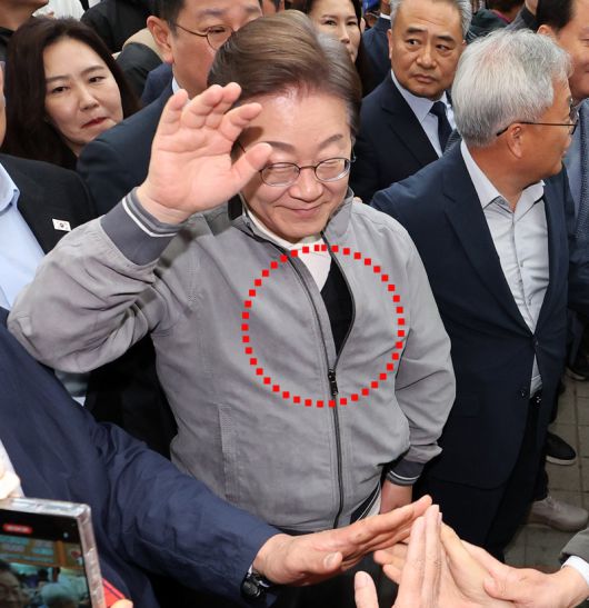 방검복 입은 李… 피습 우려에 경호도 강화 더불어민주당 이재명 대선 후보가 3일 강원 양양군 양양시장에서 상인 및 주민들에게 인사를 하고 있는 가운데, 이 후보가 점퍼 안으로 착용한 검은색 방검복(가운데 동그라미)이 보이고 있다. 이 후보 측은 피습에 대한 우려로 대선 행보 중 악수 등 대인 접촉을 최소화했다. 양양=뉴시스