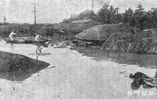 1925년 7월 13일 자. 지붕까지 물에 찬 뚝섬 지역 초가집 모습. 그 옆으로 흰 옷을 입은 두 명의 남성이 배를 타고 이동하는 듯한 모습