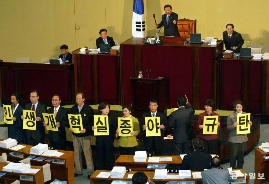 민주노동당 의원들이 국회 본회의장에서 여야 합의에 항의하는 피켓 시위를 벌이고 있는 가운데 김원기 국회의장이 본회의 개회를 선언하고 있다.  2004년 12월 31일. 동아일보 DB