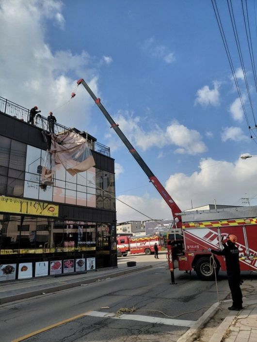 경기 고양시 일산 옥상에 설치되어 있는 캐노피 천막 구조물이 강풍으로 탈락돼 소방 당국이 크레인을 활용해 지상으로 인양 작업을 벌이고 있다. (경기소방재난본부 제공) 뉴스1