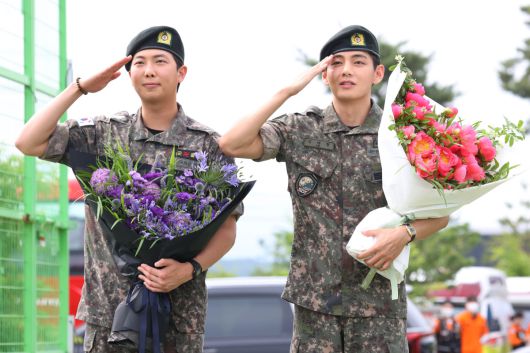 육군 현역 복무를 마치고 만기 전역한 그룹 방탄소년단(BTS) RM과 뷔가 10일 강원 춘천시 신북읍체육공원에서 취재진을 향해 거수경례하고 있다. (연합뉴스)