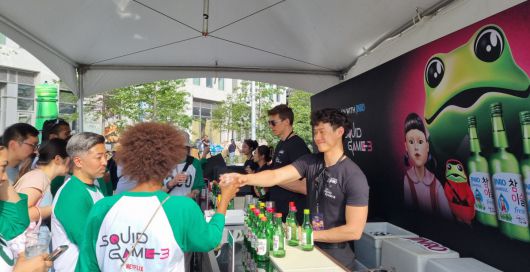 오징어게임 컬래버 제품 출시와 관련해, 27일 행사장에서 'Squid Game' 문구가 적힌 옷을 입은 사람들이 소주 병이 진열된 테이블 앞에서 프로모션에 참여하고 있다.