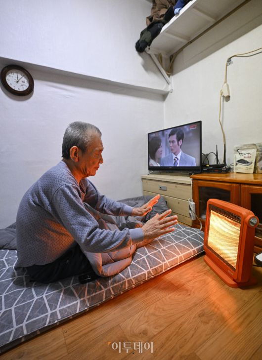 영하 10도 안팎의 한파가 닷새째 이어진 23일 서울 용산구 동자동 쪽방촌에서 한 주민이 이불과 전기난로로 추위를 피하고 있다. 조현호 기자 hyunho@