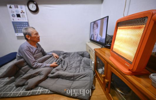 영하 10도 안팎의 한파가 닷새째 이어진 23일 서울 용산구 동자동 쪽방촌에서 한 주민이 이불과 전기난로로 추위를 피하고 있다. 조현호 기자 hyunho@