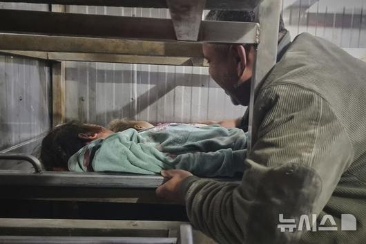 [가자지구=AP/뉴시스] 18일(현지 시간) 가자지구 남부 칸 유니스 병원 영안실에서 한 남성이 이스라엘군 공습으로 숨진 아이의 시신을 안치하고 있다. 2025.03.18.