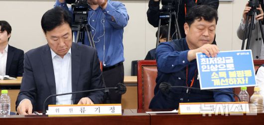 [세종=뉴시스] 강종민 기자 = 22일 세종시 정부세종청사에서 열린 최저임금위원회 제1차 전원회의에서 류기섭 근로자 위원이 최저임금 인상 피켓을 책상에 올리고 있다. 왼쪽은 류기정 사용자 위원. 2025.04.22. ppkjm@newsis.com