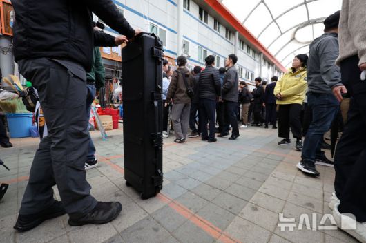[양양=뉴시스] 조성우 기자 = 민심을 청취하는 '경청 투어'에 나선 이재명 더불어민주당 대선후보가 3일 강원도 양양군 양양시장에서 상인 및 주민들에게 인사를 하는 가운데 경호 관계자가 안티드론건 가방을 들고 있다. 이 후보 측은 "후보에 대한 피습 모의 제보가 잇따르고 있다"고 밝혔다. 2025.05.03. xconfind@newsis.com