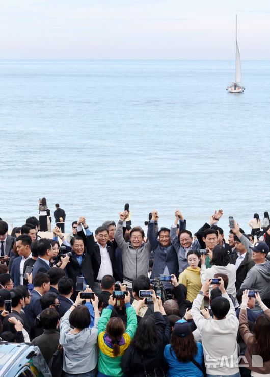 [강릉=뉴시스] 조성우 기자 = 민심을 청취하는 '경청 투어'에 나선 이재명 더불어민주당 대선후보가 3일 강원도 강릉시 안목해변 카페거리에서 이병주 의원, 이 후보 직속 이광재 국가미래정책위원회 공동위원장 등과 손을 맞잡고 주민들과 관광객들에게 인사하고 있다. 2025.05.03. xconfind@newsis.com