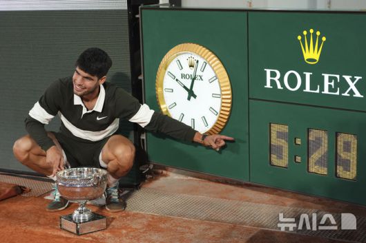 [파리=AP/뉴시스] 카를로스 알카라스(2위·스페인)가 8일(현지 시간) 프랑스 파리 롤랑가로스에서 열린 프랑스오픈 남자 단식 정상에 올라 트로피를 들고 경기 진행 시간을 보여주는 시계를 가리키며 포즈를 취하고 있다. 알카라스는 결승전에서 얀니크 신네르(1위·이탈리아)와 5시간 29분 대접전 끝에 3-2(4-6 6-7 6-4 7-6 7-6) 역전승을 거두고 대회 2연패를 달성했다. 2025.06.09.