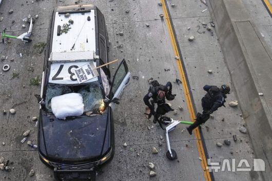 [로스앤젤레스=AP/뉴시스] 8일(현지 시간) 미 캘리포니아주 로스앤젤레스 도심 메트로폴리탄 구치소 인근 101번 고속도로에서 경찰관 두 명이 이민세관단속국(ICE)의 불법 이민자 단속에 항의해 시위대가 던지는 돌과 스쿠터를 피하고 있다. 2025.06.09.