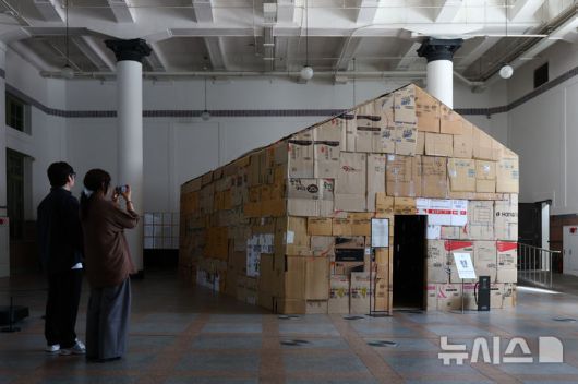 [서울=뉴시스] 황준선 기자 = 12일 서울 용산구 문화역서울 284에서 열린 '우리들의 낙원' 사전 공개 행사에서 관람객들이 이원호 작가의 '부(浮) 부동산' 작품을 관람하고 있다. 오는 13일 개막하는 '우리들의 낙원' 전시는 행복과 이상향을 주제로 하여 과거 사람들이 서울역에서 품어왔던 출발, 설렘, 시대, 위안 등 장소성을 되새기며 행복과 이상향을 탐구하는 여정을 VR, 사진, 설치, 영상 등 50여가지 작품으로 선보인다. 2025.06.12. hwang@newsis.com