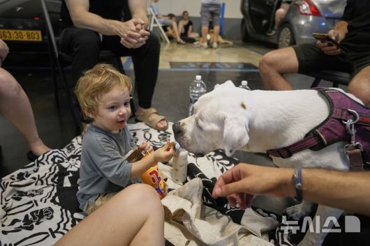 [텔아비브=AP/뉴시스] 15일(현지 시간) 이스라엘 텔아비브에 이란의 미사일 경보가 발령된 가운데 한 주차장 대피소에 가족과 함께 대피한 아이가 개에게 먹이를 주고 있다. 2025.06.16.