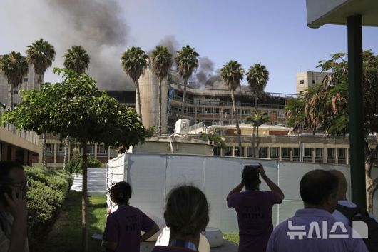 [베르셰바=AP/뉴시스] 19일(현지 시간) 이스라엘 베르셰바에서 시민들이 이란의 미사일 공격으로 연기가 치솟는 소로카 병원을 지켜보고 있다. 이란 혁명수비대는 “병원 근처 이스라엘군 지휘·정보센터가 타격받았다”라고 주장했다. 2025.06.20.