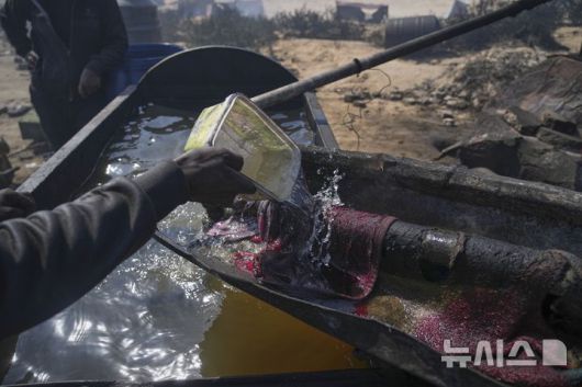 [가자시티=AP/뉴시스] 지난 22일(현지 시간) 가자지구 가자시티 남쪽 시로드에서 팔레스타인인이 플라스틱에서 추출한 연료를 식히기 위해 물을 사용하고 있다. 팔레스타인 청년들은 플라스틱 폐기물을 금속 드럼에 넣고 가열해 만든 연료를 병에 담아 판매하며, 이는 현지에서 발전기나 이동용 연료로 사용된다. 유독한 연기와 불길에 노출되는 고된 작업이지만, 이들에게는 가족의 생계를 이어가는 거의 유일한 수단이다. 2025.06.25.