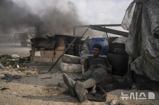 [가자시티=AP/뉴시스] 지난 22일(현지 시간) 가자지구 가자시티 남쪽 시로드에서 모하메드 나짐이라는 팔레스타인 청년이 플라스틱을 녹여 연료를 추출하는 작업 중 휴식하고 있다. 팔레스타인 청년들은 플라스틱 폐기물을 금속 드럼에 넣고 가열해 만든 연료를 병에 담아 판매하며, 이는 현지에서 발전기나 이동용 연료로 사용된다. 유독한 연기와 불길에 노출되는 고된 작업이지만, 이들에게는 가족의 생계를 이어가는 거의 유일한 수단이다. 2025.06.25.