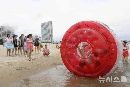 [원산=AP/뉴시스] 지난 2일 북한 강원도 원산의 원산-갈마 해안관광지구에서 사람들이 대형 물풍선 속에서 구르며 물놀이를 즐기는 남성들을 바라보고 있다. 북한 노동신문은 갈마관광지구 개장을 알리며 "세상에 없는 황홀한 관광 명소"라고 선전했다. 원산 명사십리 해변 일대에 조성된 관광지구 개발은 북한이 11년간 공들인 숙원사업으로 알려져 있다. 2025.07.04.