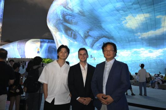 [서울=뉴시스] 오픈AI가 서울디자인재단과 협력해 세계 최대 규모의 비정형 건축물 3D 미디어 파사드 축제인 '서울라이트 DDP 2025 가을'에 참여했다. 오픈AI 지원을 받은 최세훈 작가(왼쪽)가 인공지능(AI) 영상 생성 도구 '소라'로 제작한 미디어 아트 'The Valley and the light' 앞에서 제이크 윌크진스키 오픈AI 아시아태평양 지역 커뮤니케이션 총괄(가운데)과 최강희 서울디자인재단 대표이사와 함께 기념사진을 찍었다. (사진=최세훈 작가 제공) *재판매 및 DB 금지