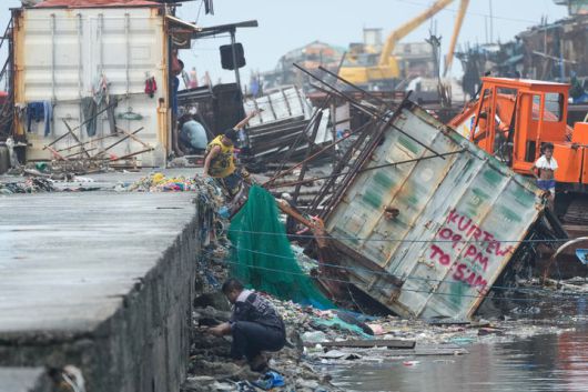 [나보타스=AP/뉴시스] 10일(현지 시간) 필리핀 해안 마을 나보타스에서 한 남성이 제26호 태풍 '풍웡'의 영향으로 뒤집힌 컨테이너 화물차 옆을 뛰어넘고 있다. 필리핀에 제25호 태풍 '갈매기'에 이어 불과 닷새 만에 26호 태풍이 상륙해 또 다른 피해가 잇따르고 있다. 2025.11.10.